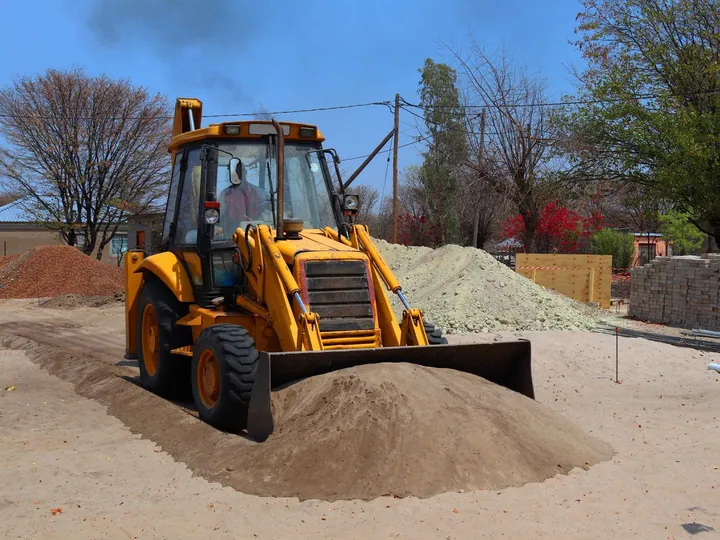 Yellow backhoe loader moving soil at a construction site
