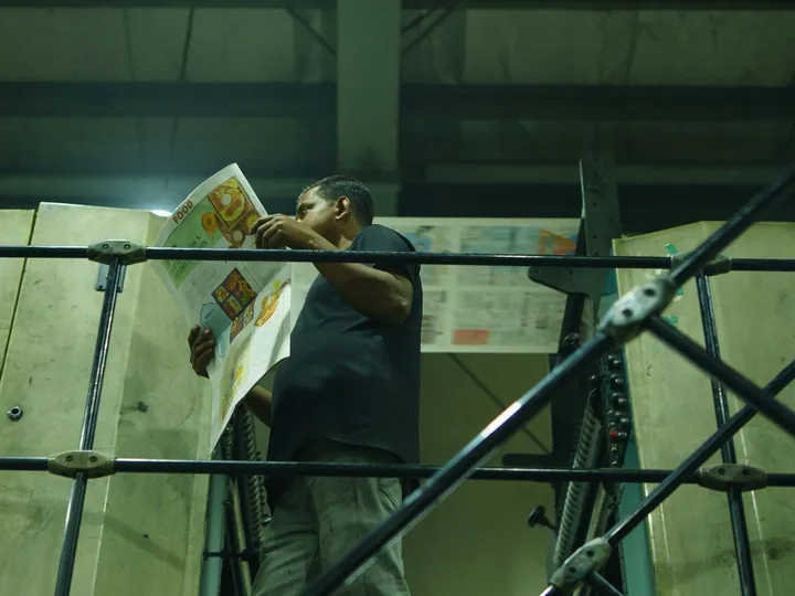 Worker inspecting printed newspaper beside industrial printing equipment